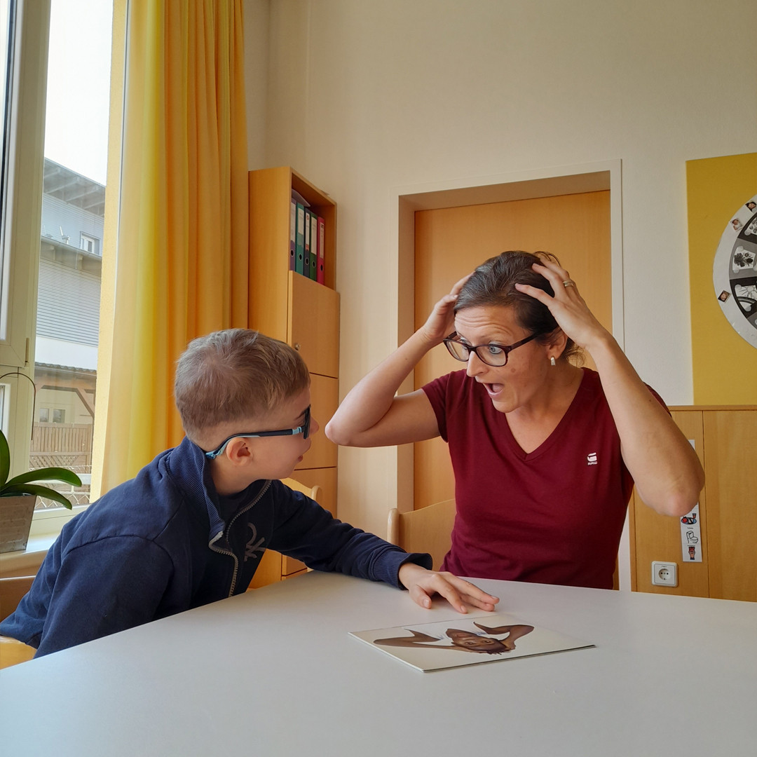 Hortbetreuerin sitzt mit einem Kind am Tisch und spricht über Gefühle.