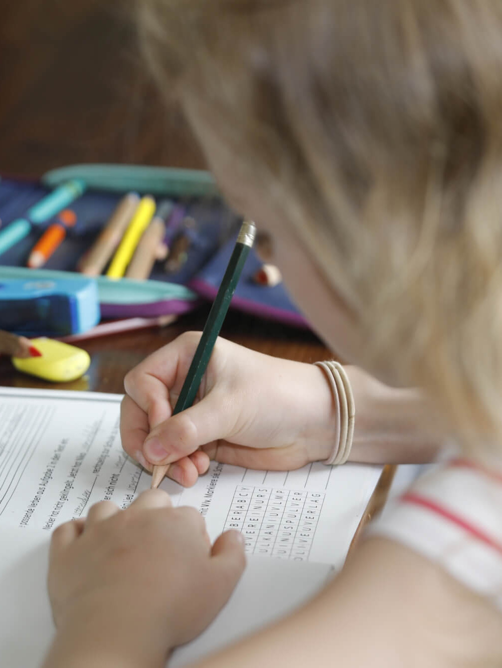 Mädchen sitzt an einem Tisch und schreibt mit Bleistift auf ein Arbeitsblatt