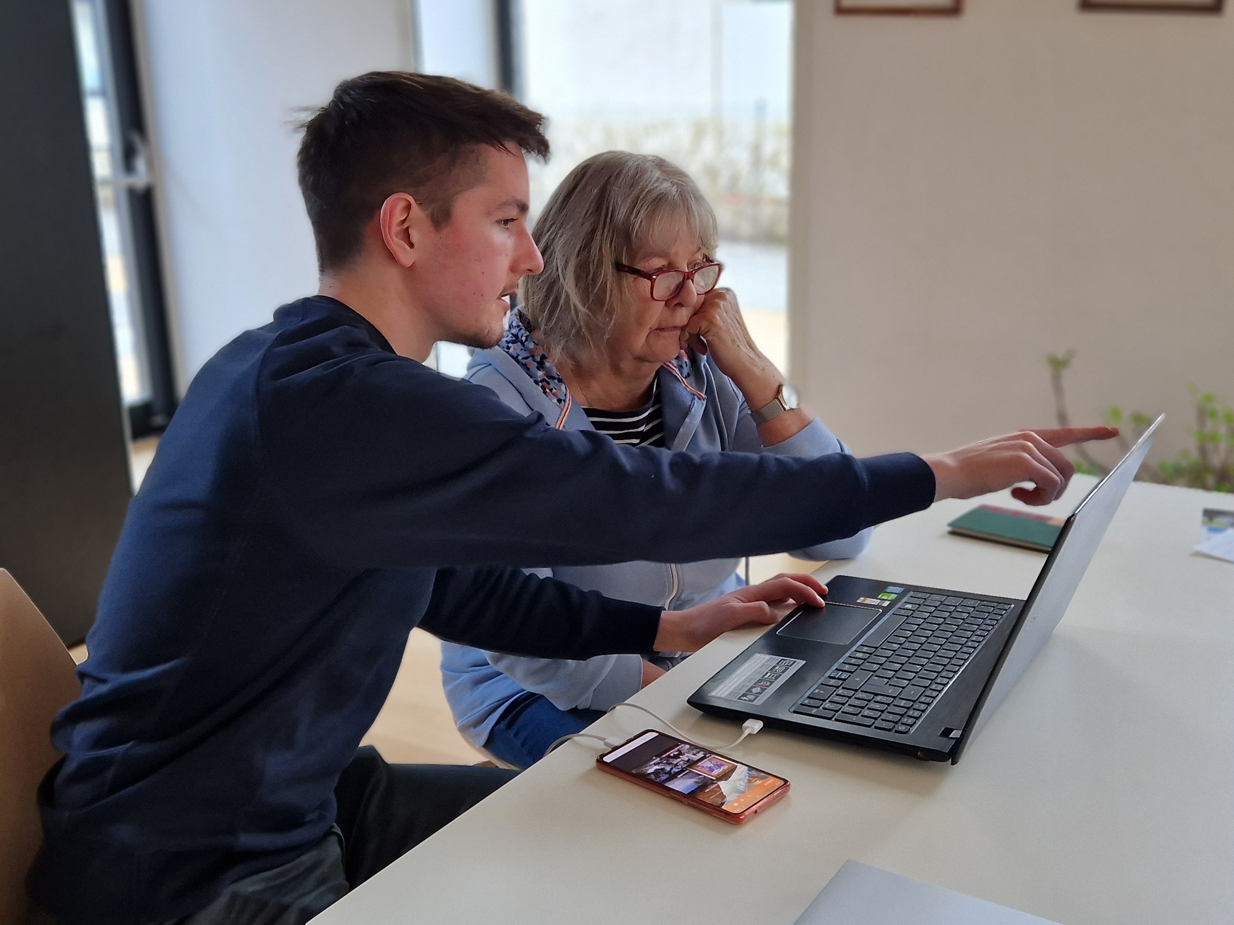 Ein Freiwilliger zeigt einer Seniorin etwas auf einem Laptop.