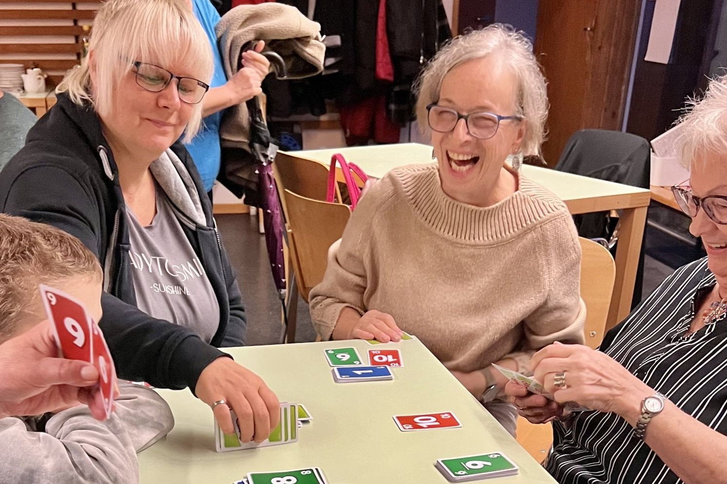 Drei Frauen und ein Bub sitzen an einem Tisch und spielen Uno