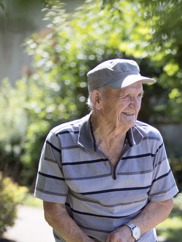Eine Mitarbeiterin der Diakonie und ein älterer Mann stehen in einem Garten und unterhalten sich freudig.