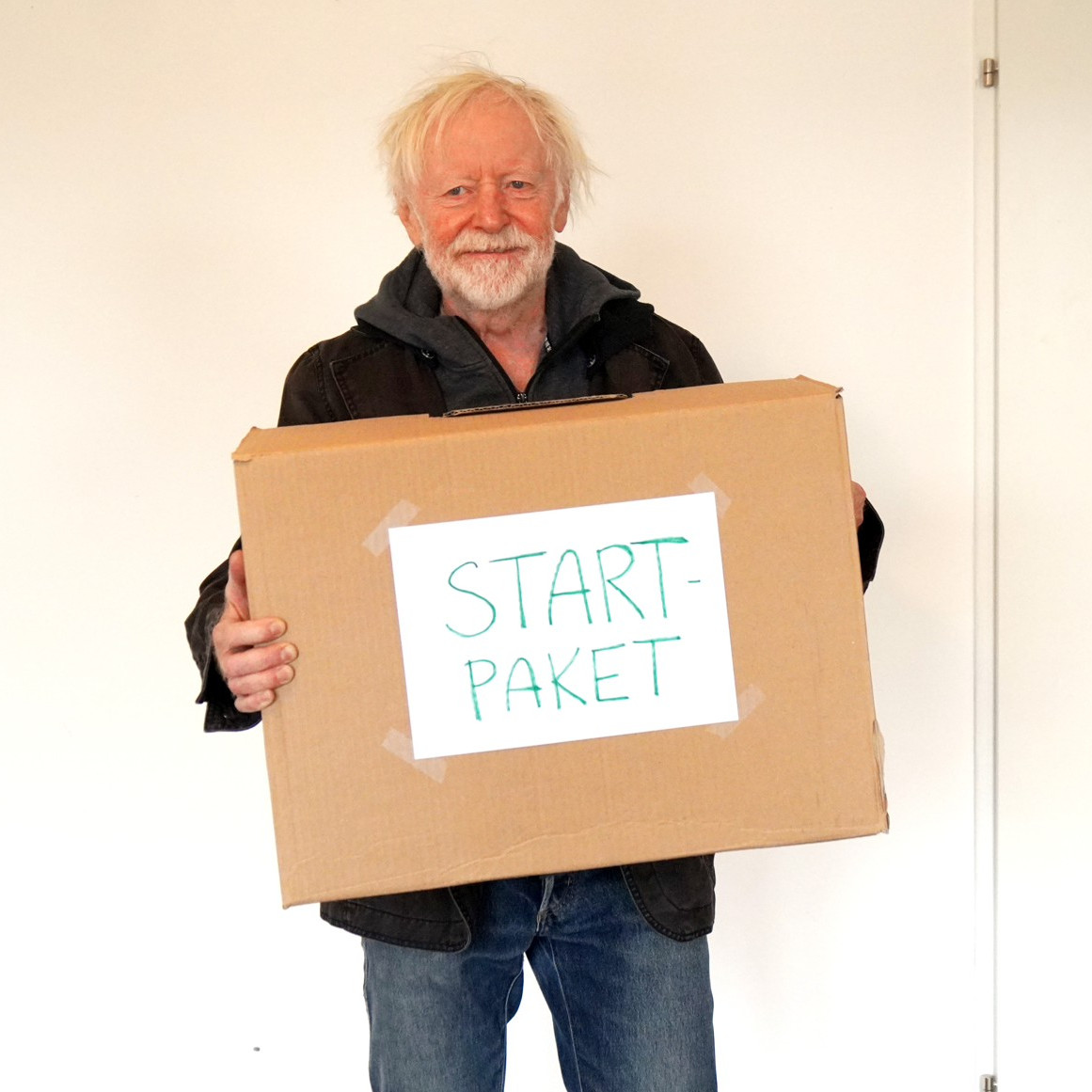 Ein Mann mit einem Umzugskarton wo "Startpaket" draufsteht