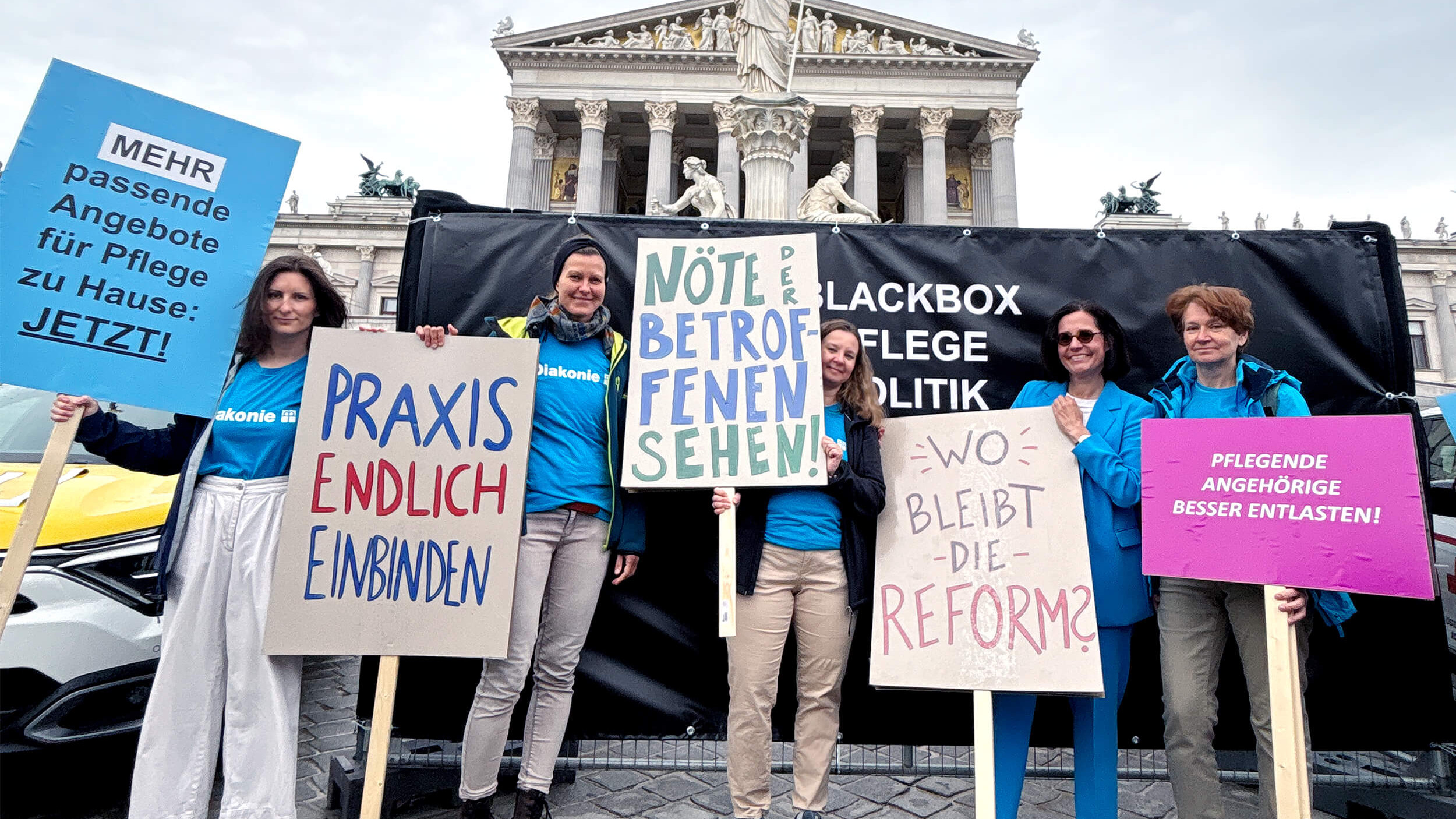 Diakonie-Mitarbeiterinnen mit Demo-Schildern vor dem Parlament