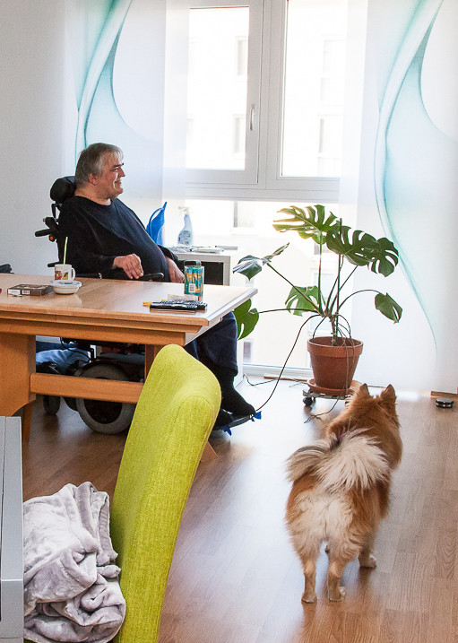 Mann im Rollstuhl wohnt alleine mit seinem Hund in seiner Wohnung.