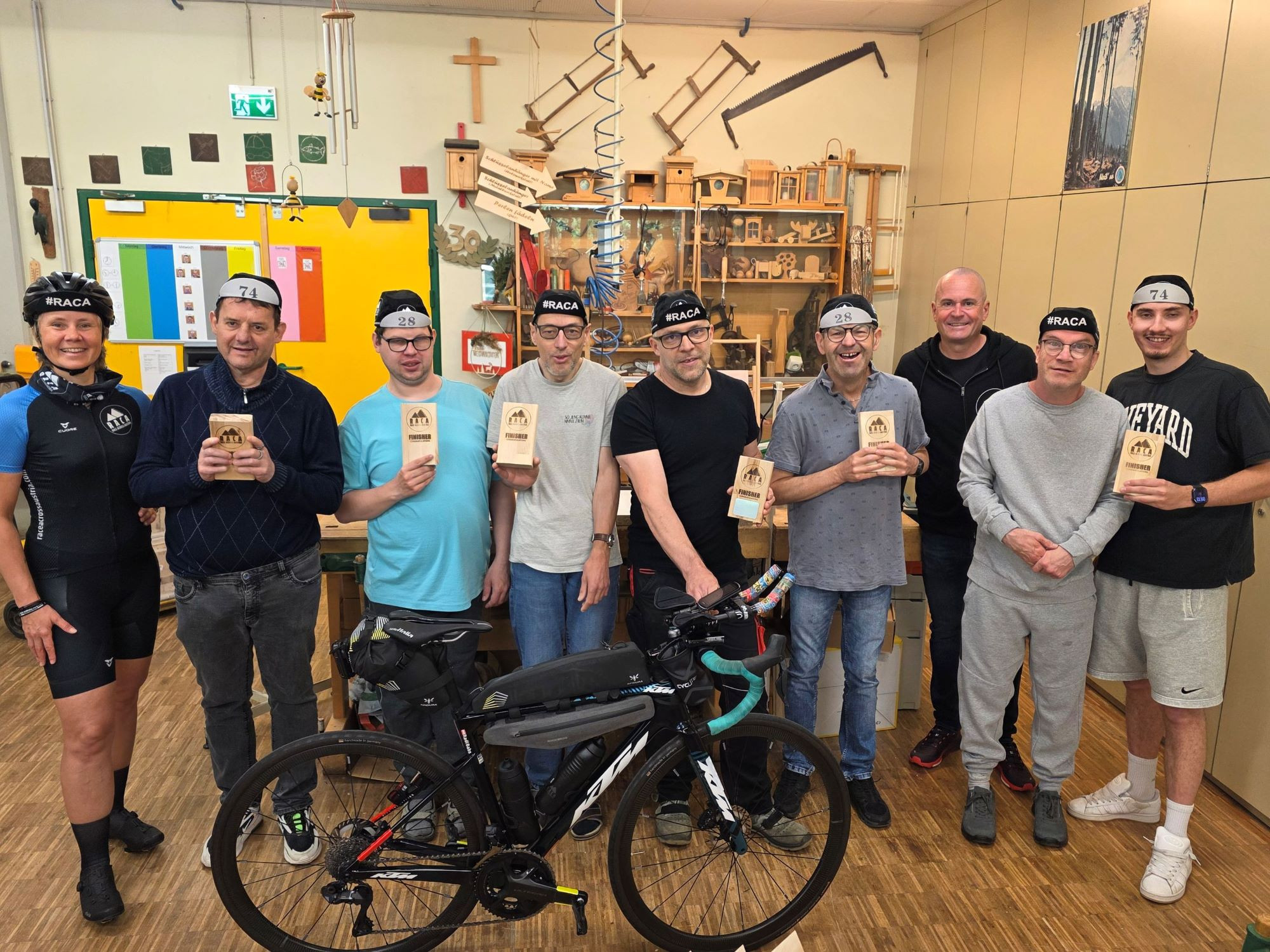 Eine Gruppe von Menschen, die eine Holztrophäe in Händen halten, davor ein Fahrrad