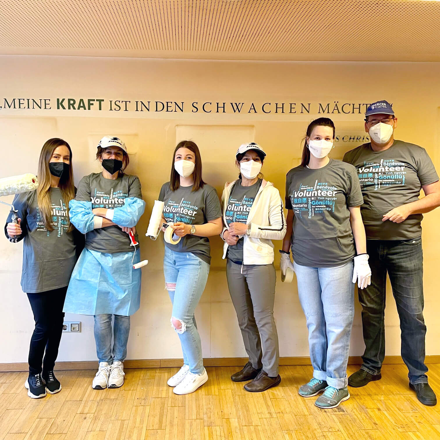 Eine Gruppe Menschen in Maleroutfits vor einer weißen Wand. Auf der Wand steht in schwarzer Schrift: Meine Kraft ist in den Schwachen mächtig.