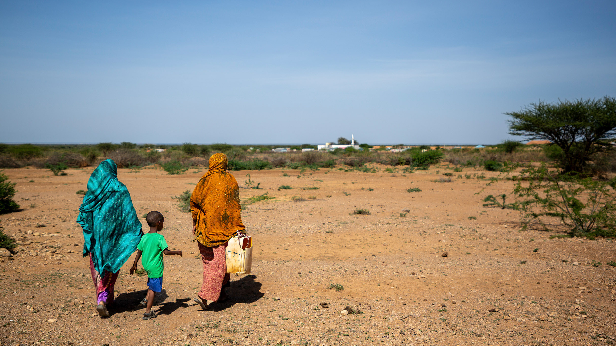 Ein Bub und zwei Frauen in einer kargen Landschaft in Somalia mit einem Wasserkanister