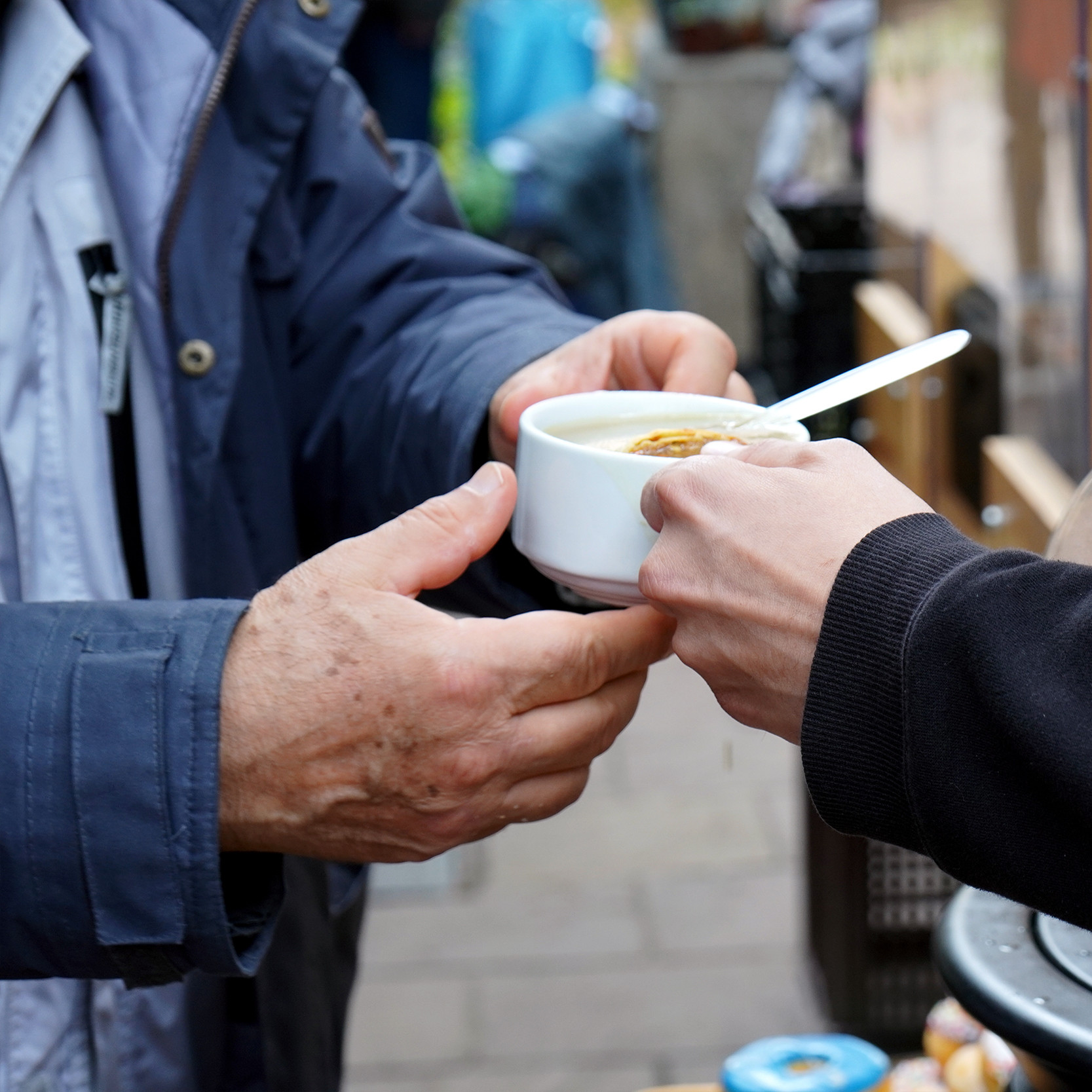 Ein Mitarbeiter im 's Häferl der Diakonie überreicht einem Gast draußen eine warme Suppe