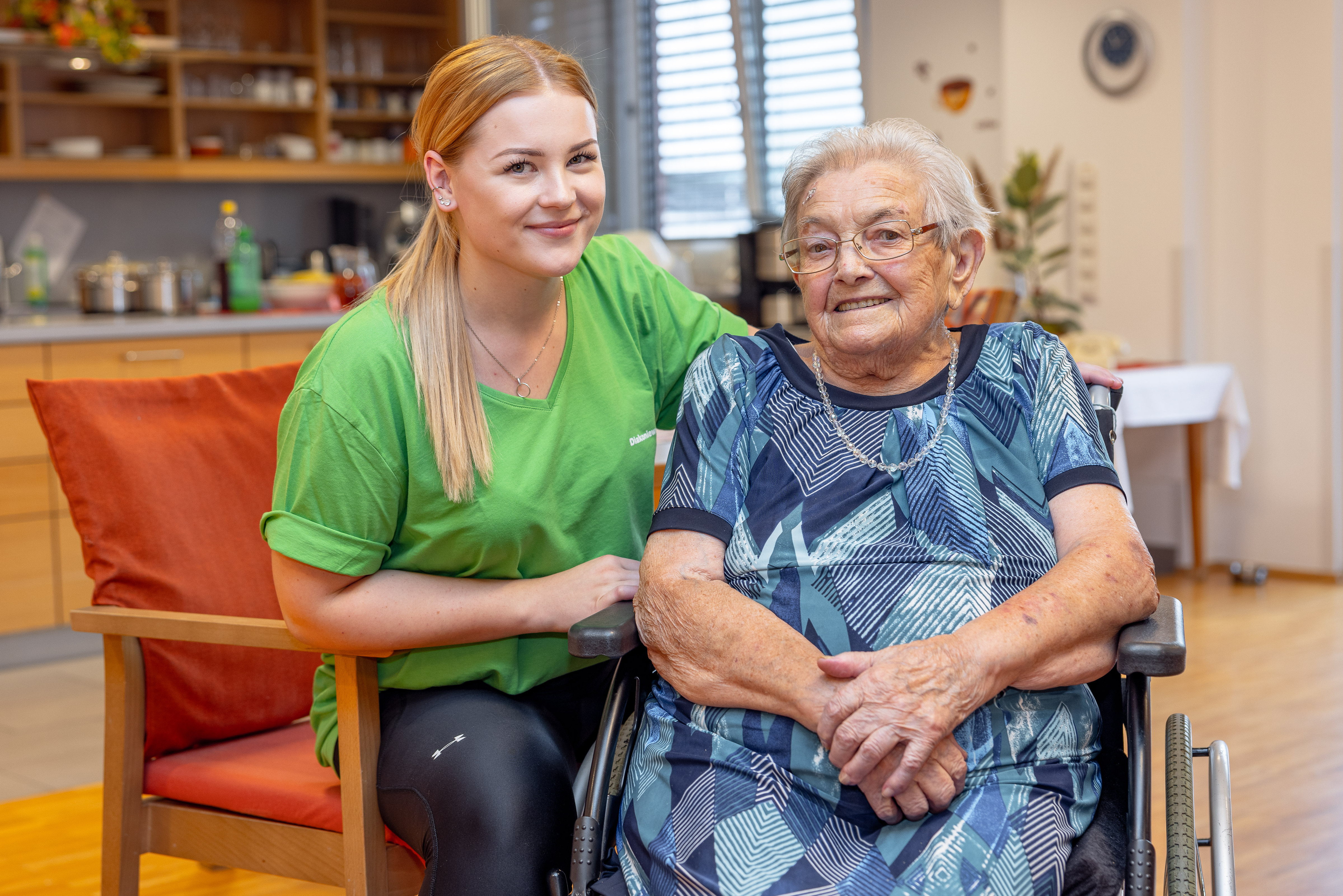 Junge und älterer Frau sitzen beisammen und lachen in die Kamera.