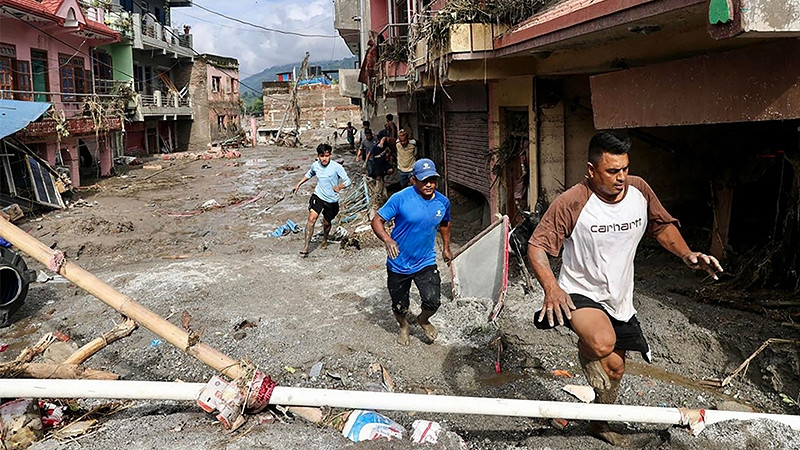 Einheimische gehen am 27. August 2026 in Devighat in der Stadt Bidur im nepalesischen Distrikt Nuwakot an Häusern vorbei, die nach Sturzfluten von Schlamm überschwemmt sind. Nach Angaben der nepalesischen Katastrophenschutzbehörde galten am 27. August noch 823 Menschen als vermisst, mehr als 24 Stunden nachdem eine tödliche Flut die Grenzregion zu Tibet heimgesucht hatte.