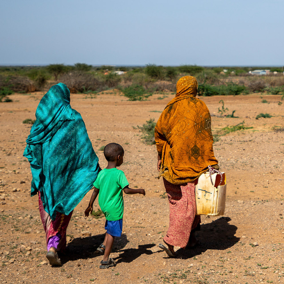 Ein Bub und zwei Frauen in einer kargen Landschaft in Somalia mit einem Wasserkanister